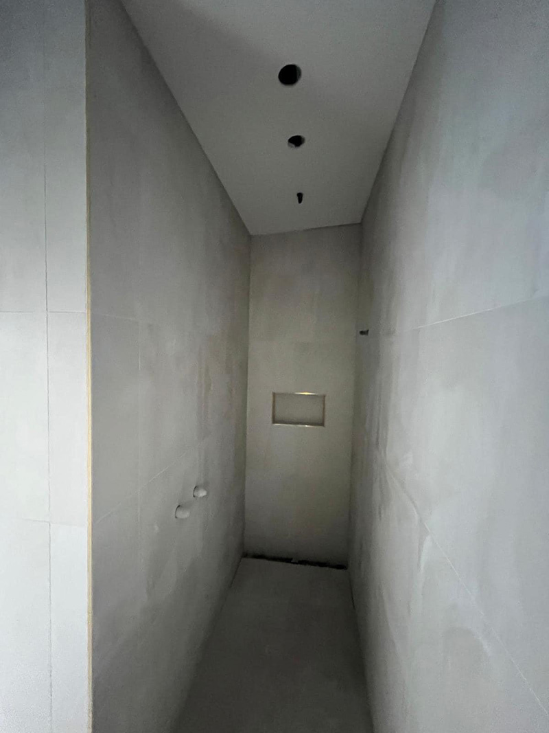Narrow room lined with large grey wall tiles and a recessed niche