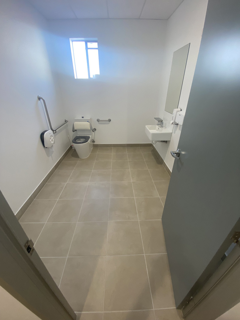 Accessible toilet with beige floor tiles and grab rails