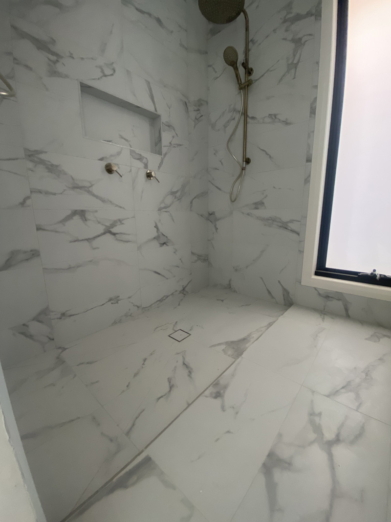Walk-in shower lined with white marble-look tiles and a wall niche