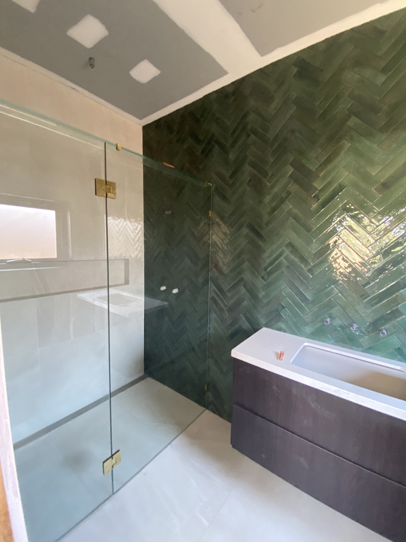 Green herringbone wall tiles in a glass shower beside a built-in bath