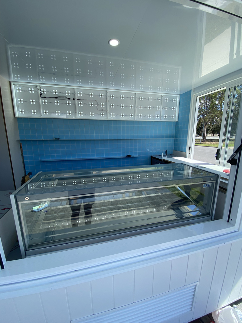 Blue wall tiles and a glass display counter seen through a servery window