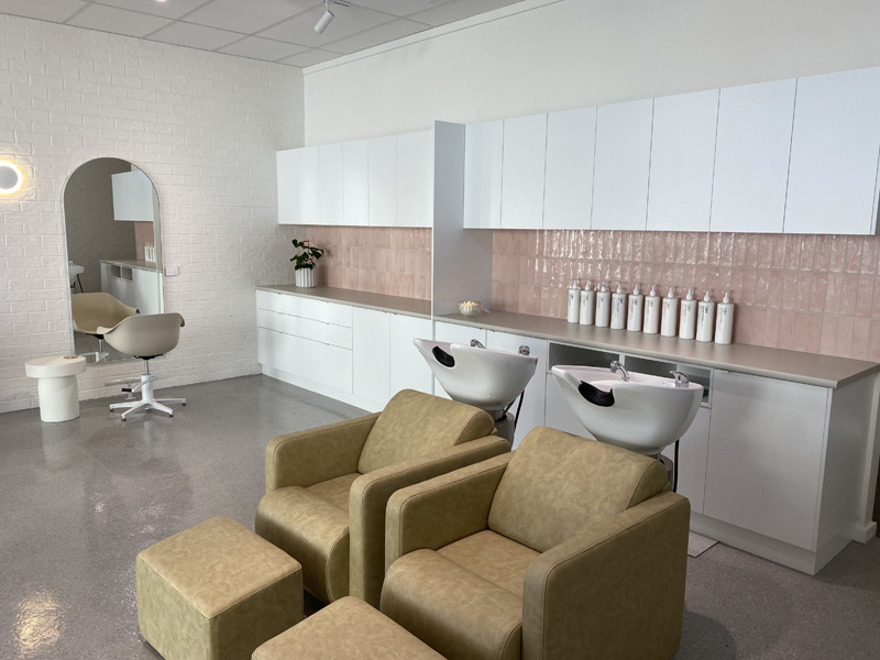 Hair salon with pink wall tiles behind wash basins, a styling chair and arched mirror