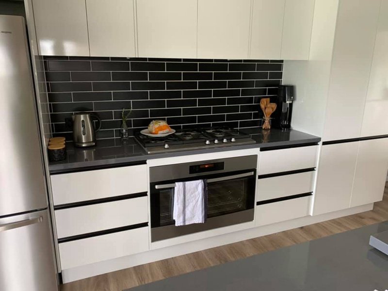 Kitchen with a black subway tile splashback, white cabinets and oven