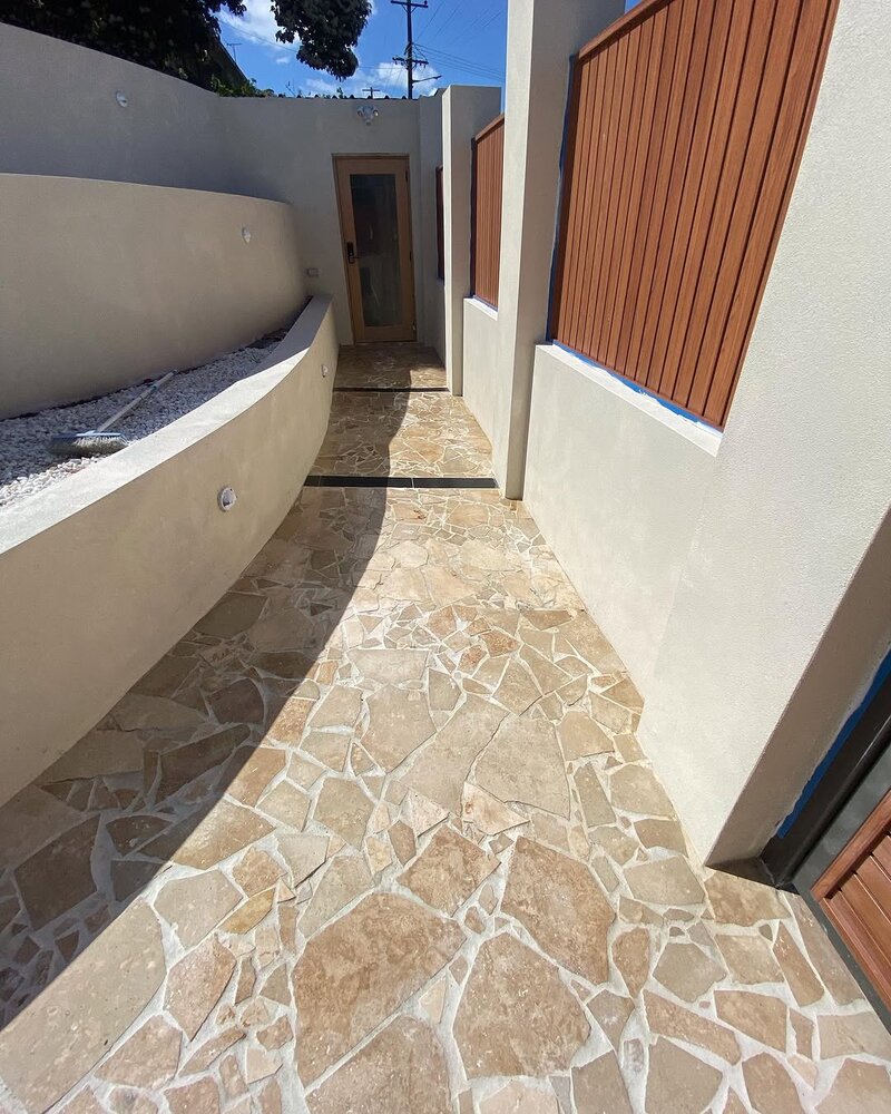 Crazy paving stone path between rendered walls and a timber fence