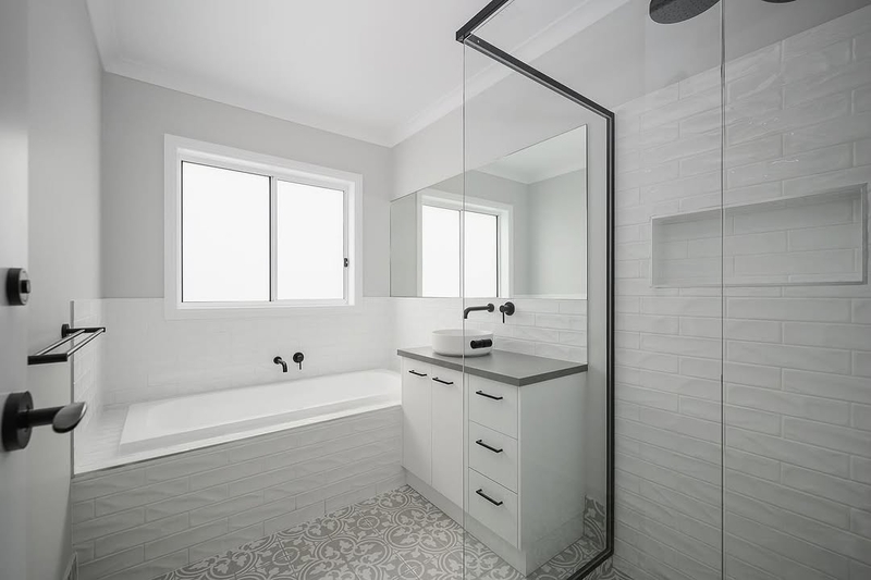 Bathroom with white wall tiles, patterned floor tiles, a bath and glass shower