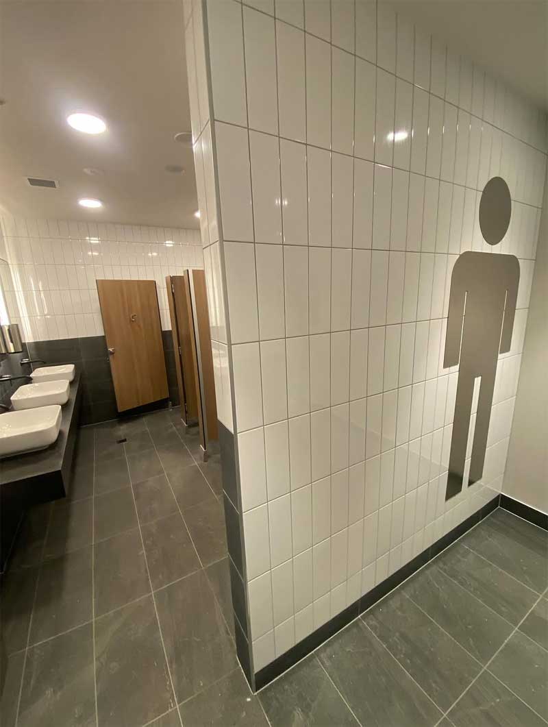 Men's toilets with white wall tiles, grey floor tiles and basins