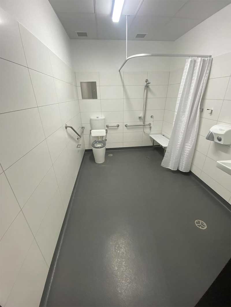 Accessible shower and toilet room with white wall tiles and grab rails