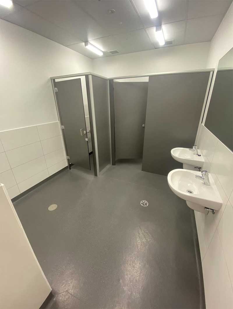 Public toilets with white wall tiles, grey floor and two basins