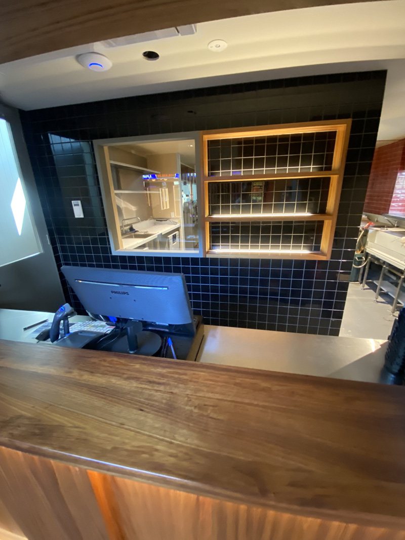 Black square wall tiles behind a timber counter and shelving
