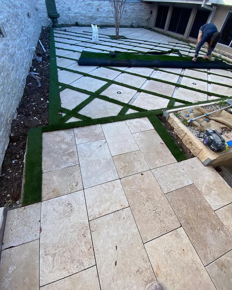 Stone pavers and artificial grass strips being laid in a courtyard
