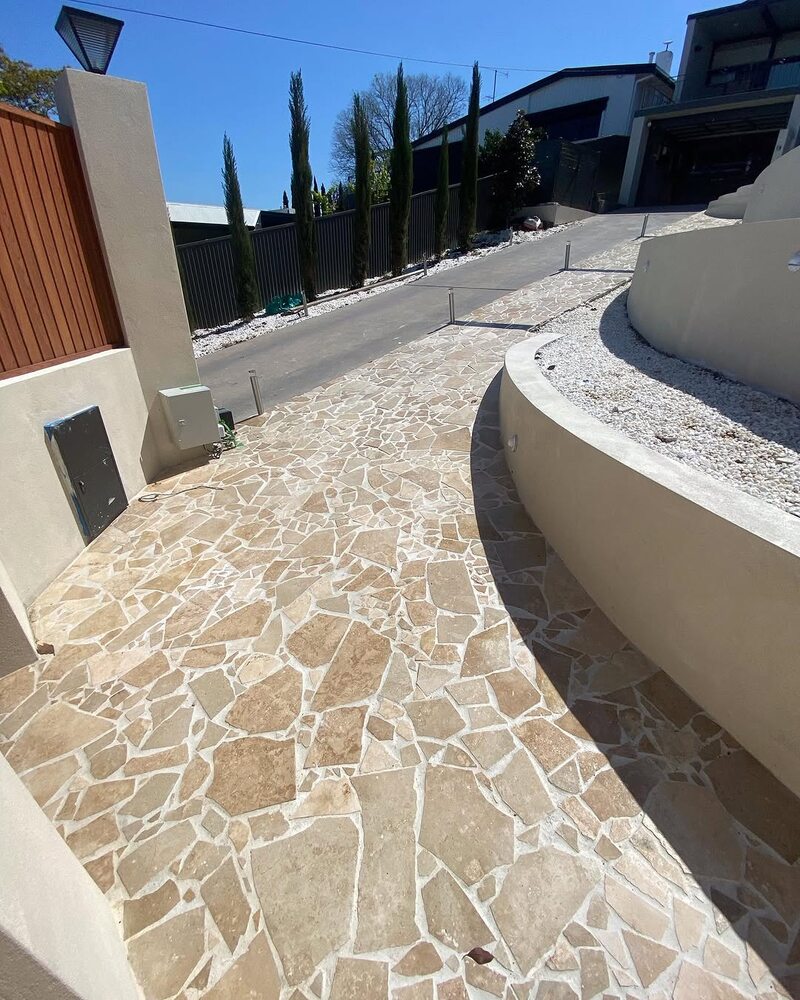 Crazy paving stone driveway curving past a rendered retaining wall