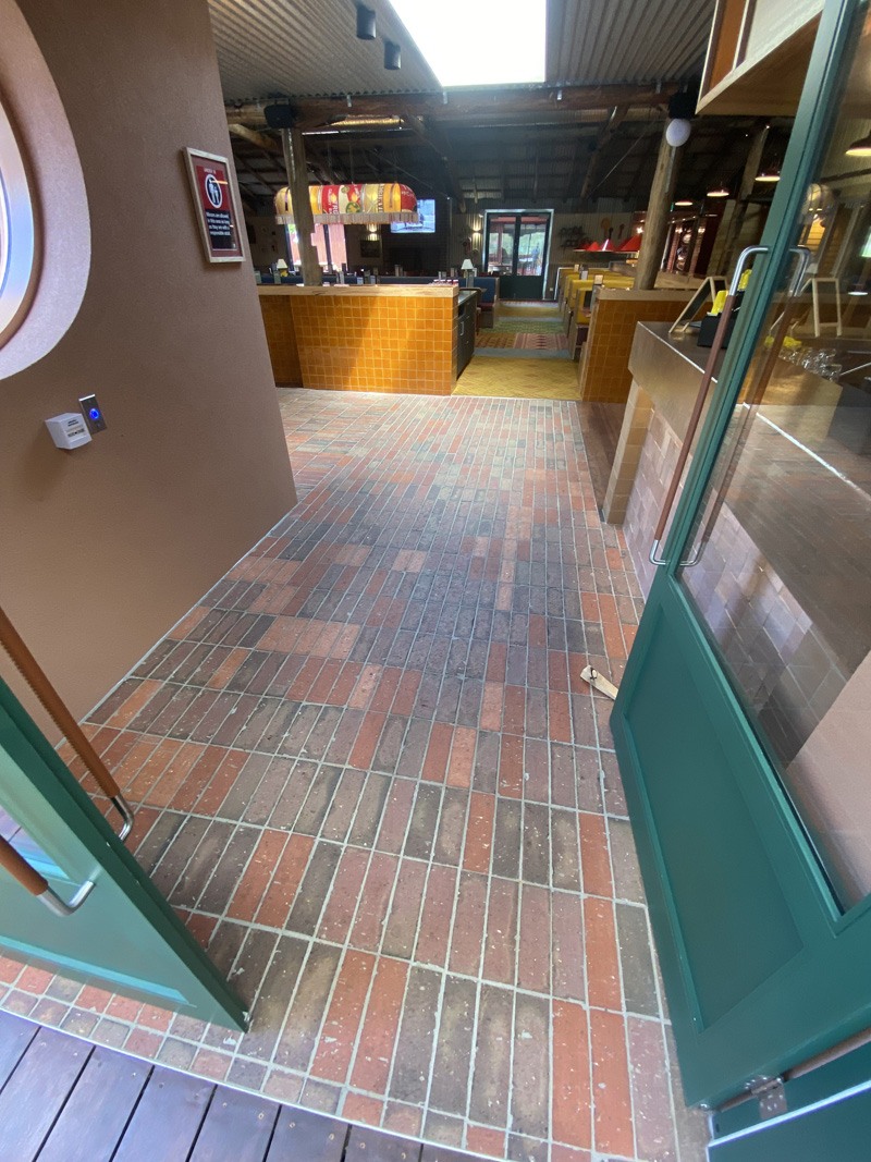 Red brick-look floor tiles through an open green door into a venue