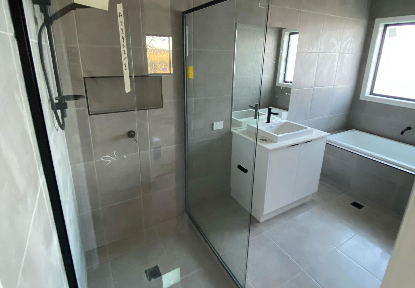 Tiled bathroom with a glass shower screen, white vanity and built-in bath