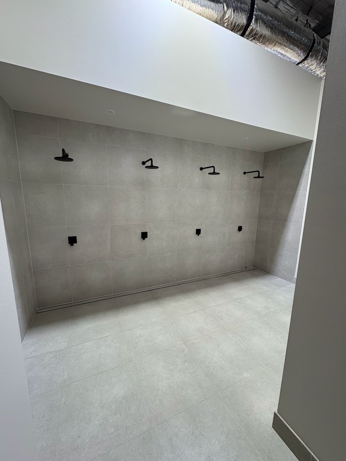 Grey tiled shower wall with four black shower heads in a row