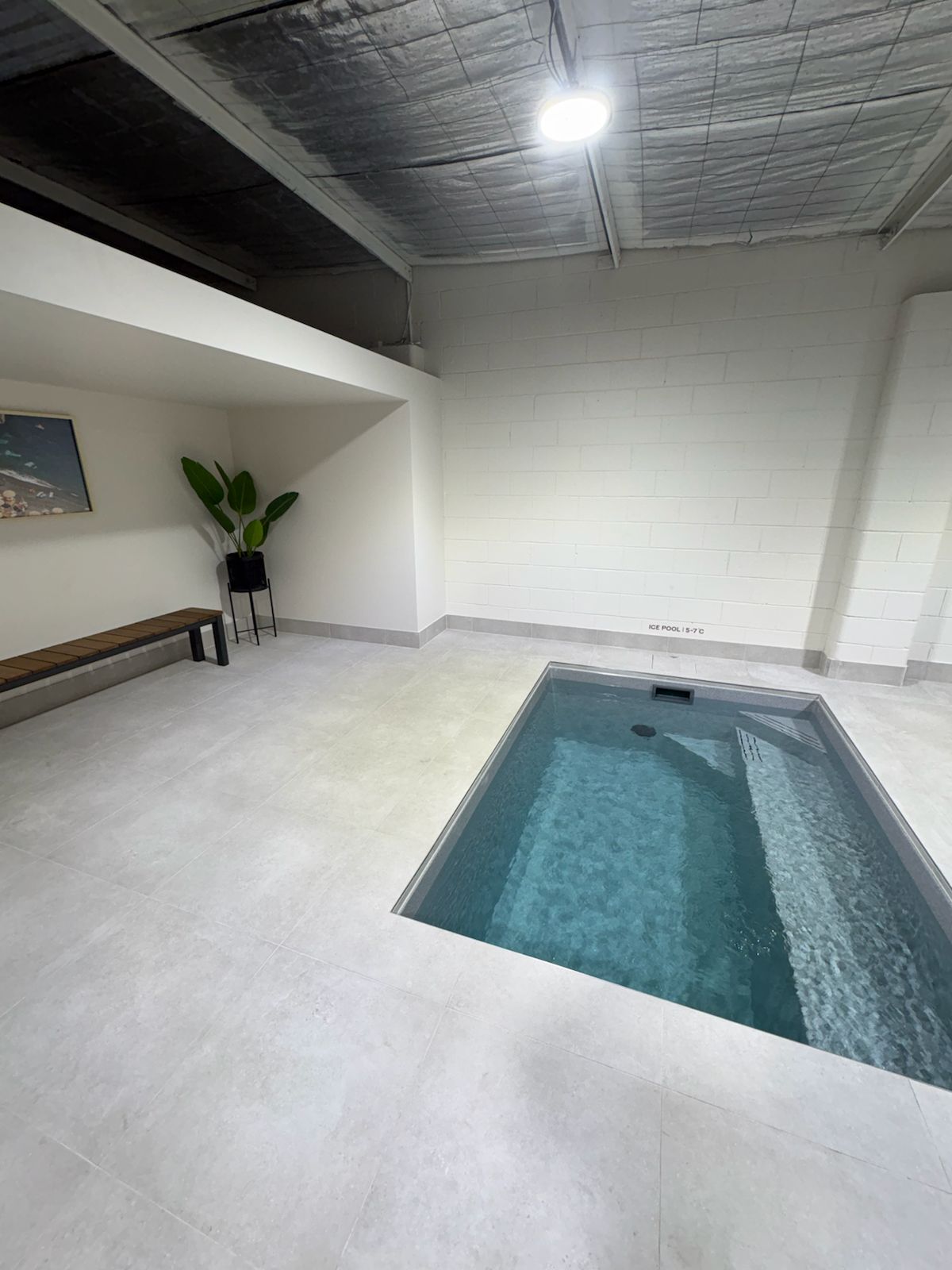 Pale floor tiles around a plunge pool beside a timber bench