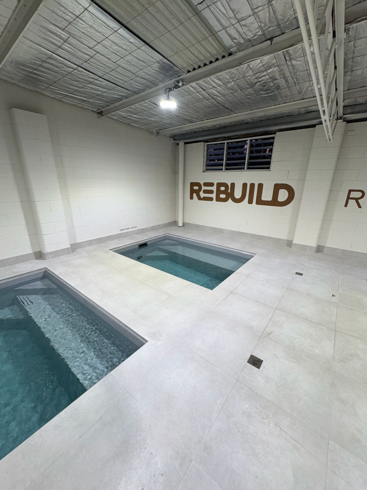 Pale tiled floor between two plunge pools below a Rebuild wall sign
