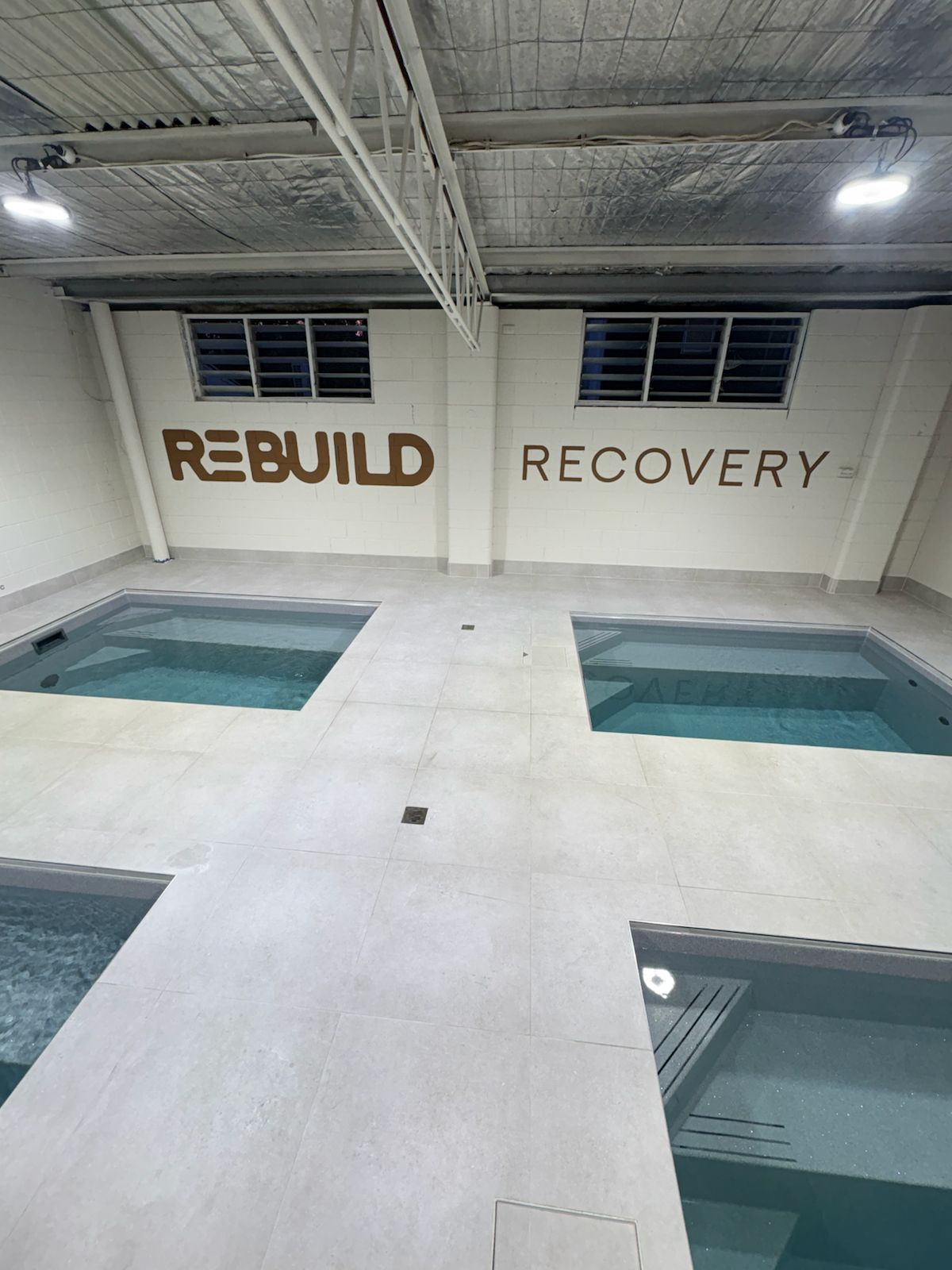 Pale floor tiles around four plunge pools under a Rebuild Recovery sign