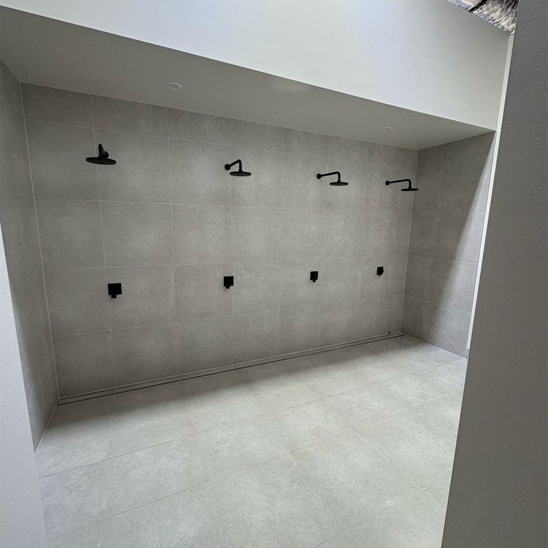 Grey tiled shower wall with four black shower heads in a row